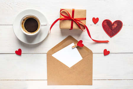 Valentines day mockup. Coffee, gift box and paper card with craft envelope on white wooden table top...