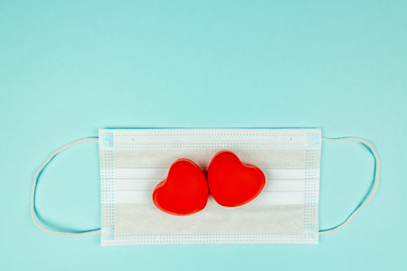 Two red hearts on medical protection mask on light blue background, top view. Concept of healthcare, self-defense. Creative flat lay with copy spaceの写真素材