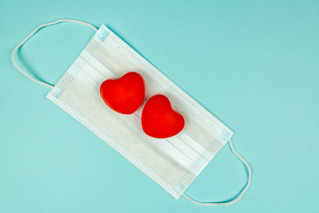 Two red hearts on medical protection mask on light blue background, top view, copy space. Concept of healthcare, self-defense.の写真素材