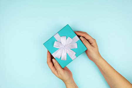 Woman holding blue gift box on color blue background. Festive greeting card. Holiday concept.