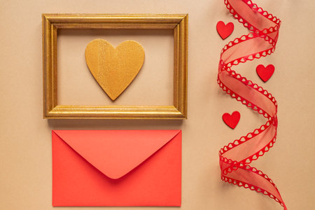 Valentine's day or Wedding romantic concept. Twisted decorative ribbon and red envelope with red hearts on beige backgroundの写真素材