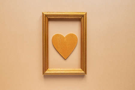Valentine's day or Wedding romantic concept. Twisted decorative ribbon and golden photo frame with wooden heart on beige backgroundの写真素材