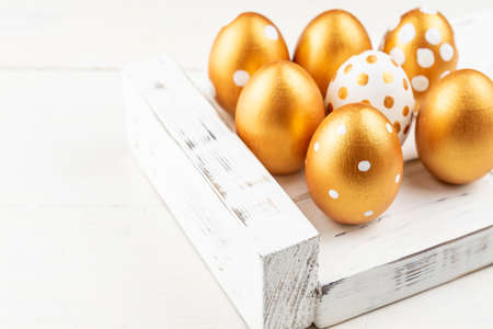 Easter festive decoration. Close up of easter eggs colored with golden paint on white wooden tray. Various dotted designs.の写真素材