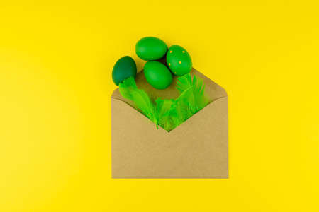 Spring Easter layout with green feathers and eggs, craft envelope on yellow background. Copy space...