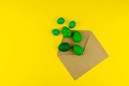 Spring Easter layout with green feathers and eggs, craft envelope on yellow background. Copy space...