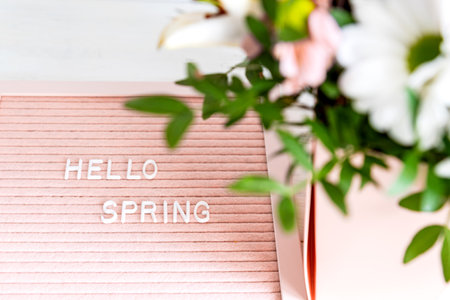 Hello Spring greeting message sign on pink felt board with blooming flowers on white background. board with text for social media blogs banner. Green leaves, natural floral bloom decorationの写真素材