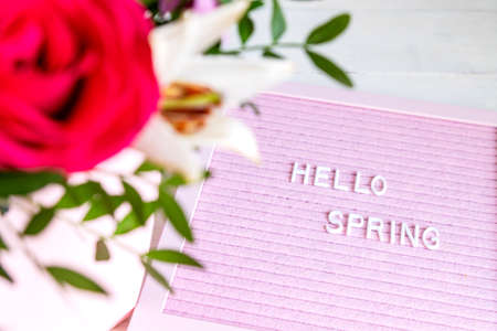 Text Hello Spring on pink letter board and bouquet of colored flowers. Concept Springtime mood and happinessの写真素材