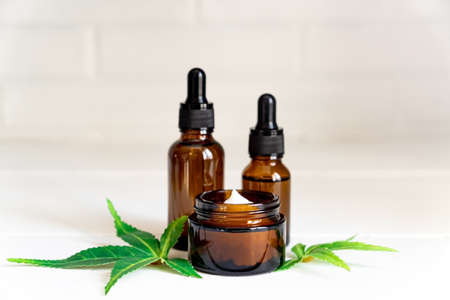 Cannabis face cream or serum or oil dropper concept. Natural cosmetic. CBD oil, THC tincture and hemp leaves on a wooden background.の写真素材