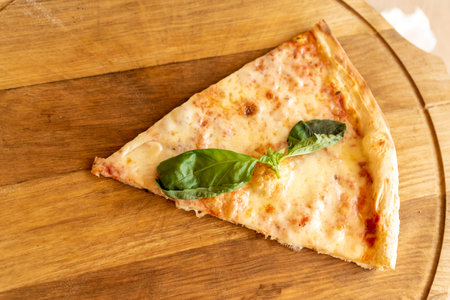 Slice of Pizza Margherita with mozzarella and basil leaves on wooden stend. Traditional italian food.の写真素材