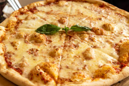 Pizza Margherita with mozzarella and basil leaves on wooden stend. Traditional italian food.