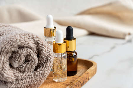 set of different bottles with beauty serum, hyaluronic acid and vitamins on wooden tray with towel. Home spa conceptの写真素材