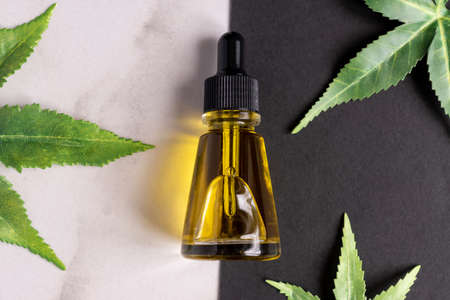Top view of Cannabis face serum or oil dropper concept. Natural cosmetic. CBD oil, THC tincture and hemp leaves on a double marble and black backgroundの写真素材