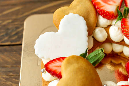 Sponge cake with strawberries, pink milk chocolate bars, silver sprinkles, vanilla cream and heart chape cookies close up. Summer sweet dessert for birthday or mothers day.の写真素材