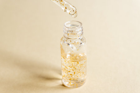 transparent bottle with beauty serum, hyaluronic acid, 24k gold and vitamins on a beige background. Luxuary home face and body care treatment concept.の写真素材