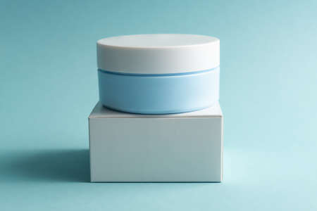 Face cream jar with plastic cap and whire carton box, package on blue background. Mockup unbranded cosmetology product.の写真素材
