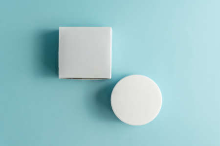 Face cream jar with plastic cap and whire carton box, package on blue background. Mockup unbranded cosmetology product.の写真素材