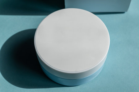 Face cream jar with plastic cap and whire carton box, package on blue background. Mockup unbranded cosmetology product.の写真素材