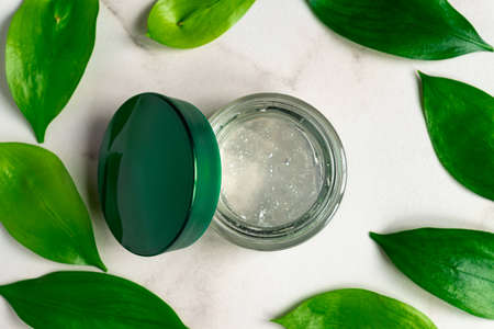 transparent jar of face cream gel on mrble background with l green leaves. top view, flat lay. Natural organic beauty product for body, hand, face skin treatment.の写真素材