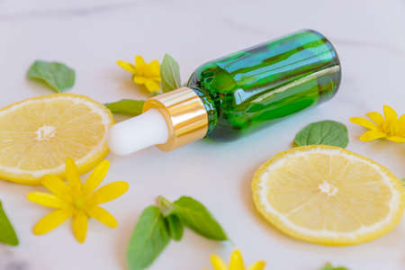 Serum with vitamin C. Lemon essential oil. green glass bottle with a pipette, slices of lemon with...
