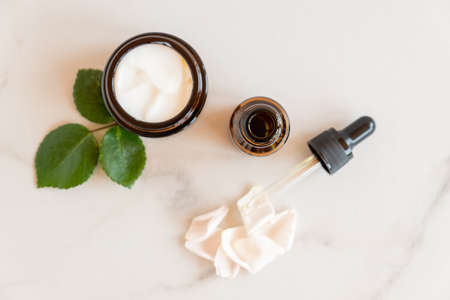 anti-aging collagen facial serum in dark glass bottle and face cream on wooden background with copy...