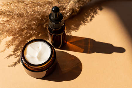 Essential oils with drops pipette and cream on baige background. Dry ear reeds or pampas grass decoration. Professional bottle for facial and body treatment. Unbranded package.の写真素材