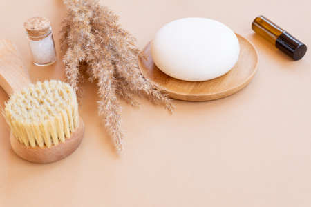 Spa and wellness concept with sea salt, dry pampas, face brush, essential oil and soap bar on beige...