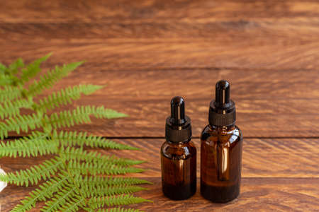 Skin care serum in amber glass dropper bottle on wooden board with fern leaves. SPA natural organic beauty product packaging designの写真素材