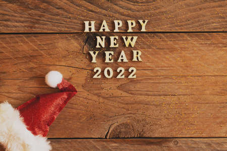 Happy new year 2022 wooden letters quote with red sparkling santa hat on wooden table with glitter....