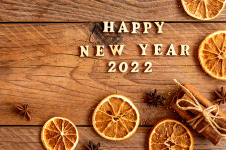 Cinnamon sticks, slices of dried orange, star anise and quote happy new year 2022 on wooden...