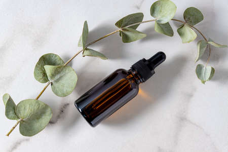 Bottle with essential oil and eucalyptus branches on marble baclground. Skin care and healthy treatment for the face and bodyの写真素材