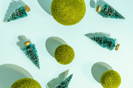 Toy christmas trees and green grass balls scattered on blue background. Conceptual pattern with hard shadows.の写真素材
