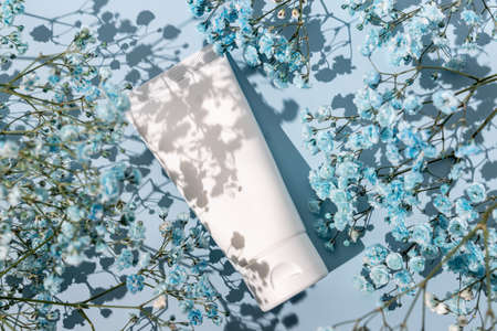 white cosmetic tube with hand cream on a blue background with blue gypsophila flowers. Cosmetics concept with herbal ingredients.の写真素材