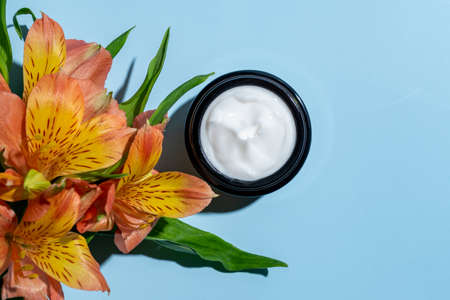 open cosmetic jars with nourishing or moisturizing cream on a blue background and alstroemeria flower with copy spaceの写真素材