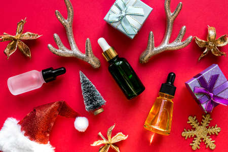 Skin care beauty products on red christmas background. Face oil in glass bottles with christmas decoration. Festive advertising.の写真素材