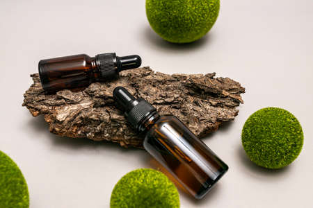Concept of natural skin care cosmetics. Essential oil or dark glass serum on a tree bark with green balls. Natural eco friendy concept for cosmetics brandの写真素材