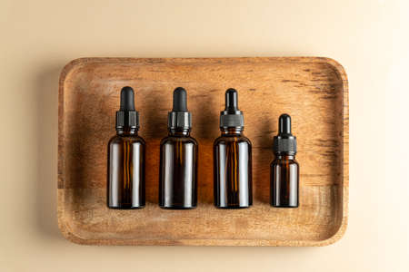 Dark glass cosmetic bottles of different size with face serum or essentioal oil on a wooden background. Unbradned Beauty cosmetic productsの写真素材