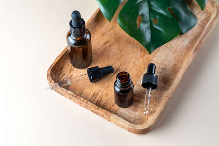 Hyaluronic acid oil, serum skin care product on beige background. Cosmetic liquid mockup in dark glasst bottle, monstera leaf decor. Mock up packaging, cosmetics design branding.の写真素材