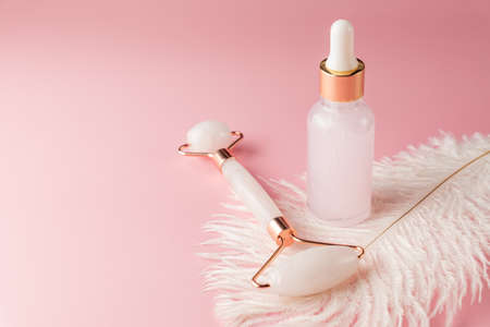 Face massaging quartz roller with beauty serum om pink background. Skin care procedures at home.の写真素材