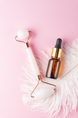 Essential face oil and quartz massaging roller on pink background. Face care routine procedures for healthy and young skin.の写真素材