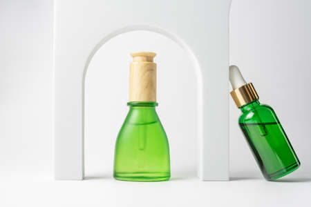 Set of natural beauty oil for skin care in green dropper bottles witb white podiums. Trendy mockup...