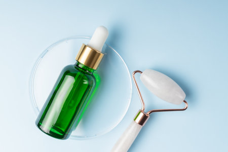 Natural face oil in green pipette bottle and quartz massaging roller on blue background. Home spa procedures presentation. unbranded package.の写真素材