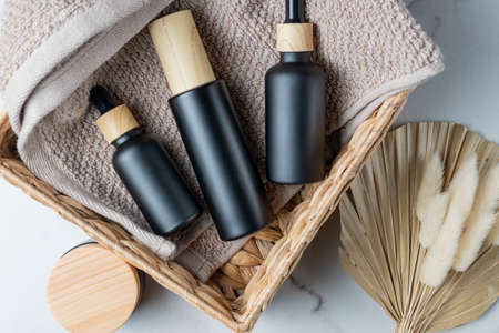 Blank black glass essential oil bottles with pipette, spray bottle and bamboo jar in recycled water lily basket with dried flowers. Organic spa cosmetic beauty product mock up. sustainable living.の写真素材