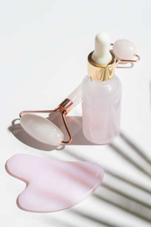 Pink Gua Sha facial massage tools. Rose Quartz jade roller and beauty facial oil on white...