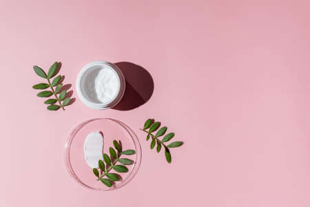 Open cream in a jar and moisturizer smear in petri dish on pink background. Beauty facial cosmetic product texture top view. Body care lotionの写真素材