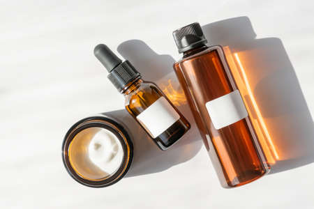 Moisturizer cream jar, serum in glass bottle and toner with green leaves on white background. Flat...