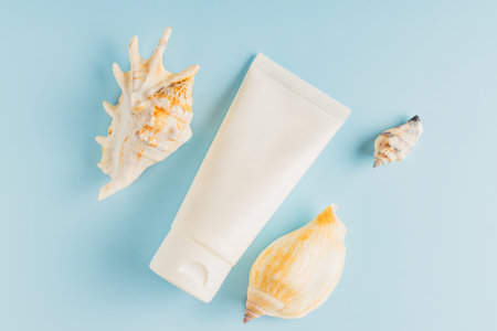 Unbranded cosmetic tube with moisturizing cream. Summer decorations, seashell on blue background. Cream or lotion. mockup style. beauty concept. top view.の写真素材