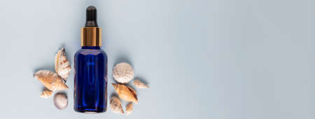 cosmetic serum for the face on a light blue background with seashells .The concept of a summer cosmetic moisturizing serum with collagen and oranic sea minerals. banner format.の写真素材