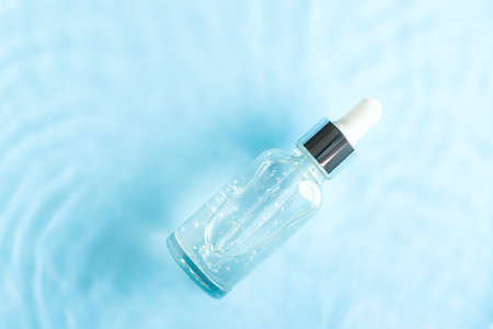 Cosmetic spa medical skin care, bottle with serum, micellar toner and essence on blue water texture background with splashes. Flat lay, copy spaceの写真素材