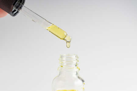 Transparent glass pipette with facial serum, bubbles on white background. medical research concept....