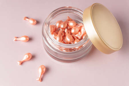 pink cosmetic capsules on pink background skattered out from a jar. Single dose serum or cream for...
